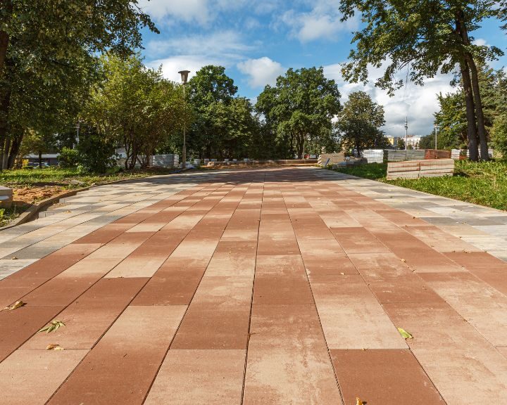 a concrete slabs walkway in a park with trees in the background.